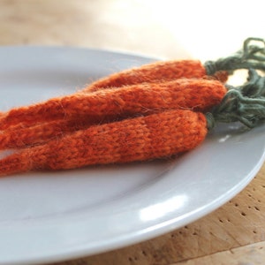 May include: A bunch of knitted orange carrots with green yarn stems on a white plate.