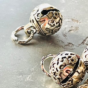 Puede incluir: Encantos de campana de plata con intrincados diseños florales. Las campanas tienen un bucle para sujetarlas a joyas u otras artesanías.