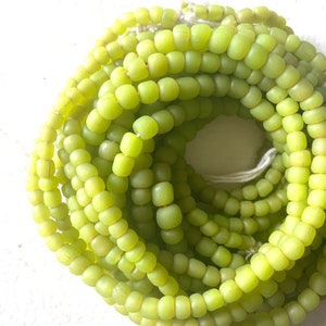 May include: A strand of lime green glass beads. The beads are small and round, and they are strung together on a white thread.