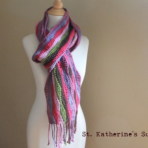 May include: A striped crocheted scarf in shades of pink, purple, green, and brown with a fringe at the bottom. St. Katherine's Supply Co.