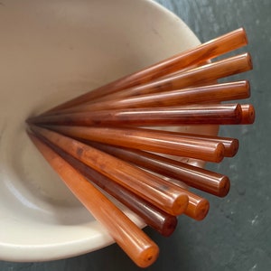 May include: A set of eight brown chopsticks in a white bowl. The chopsticks are made of a smooth, polished material and have a slightly rounded shape.