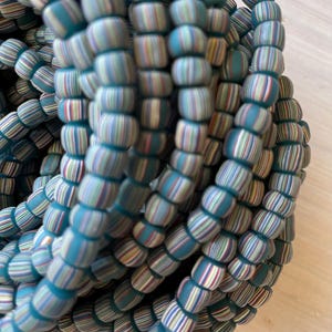 May include: A close-up of a pile of teal, white, and multi-colored striped glass beads. The beads are round and have a glossy finish.