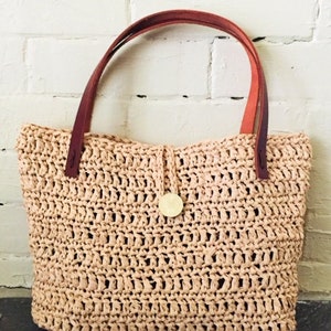 May include: A beige crocheted tote bag with brown leather handles and a gold button closure.
