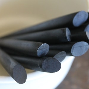 May include: A close-up of a bundle of black wooden dowels with rounded ends. The dowels are arranged in a fan shape and are in a white ceramic bowl.