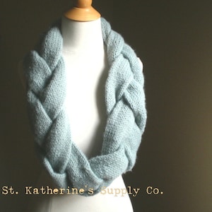 May include: A light blue knitted infinity scarf with a braided design. St. Katherine's Supply Co.