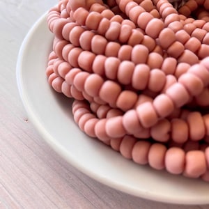 Könnte beinhalten: Nahaufnahme eines Stapels rosa Glasperlen. Die Perlen sind klein und rund und in einem zufälligen Muster angeordnet. Die Perlen liegen auf einer weißen Oberfläche.