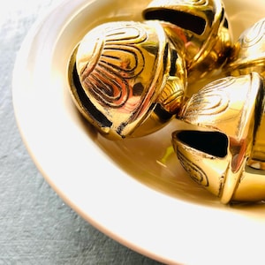 May include: Four gold-colored bells with intricate designs on a white plate. The bells are arranged in a cluster, with the tops of the bells facing the viewer.