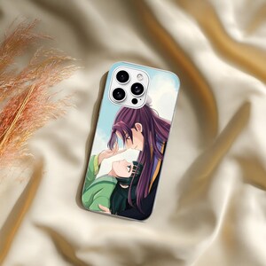 May include: A rectangular smartphone case featuring a printed anime-style illustration of two characters. One character has long dark purple hair and wears dark clothing, while the other has dark hair and wears a green garment. The background is light blue.