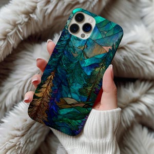 May include: A smartphone case featuring a stained-glass style forest scene with teal, blue, and gold tones. The design includes stylized trees, mountains, and a mosaic-like sky. The case has a glossy finish and a camera cutout.