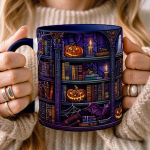 Op de afbeelding: Een keramische mok met een donkerpaarse en zwarte illustratie van een griezelige boekenplank. Het ontwerp bevat gloeiende oranje pompoenen, brandende kaarsen, een wit spook, een paarse vleermuis en spinnenwebben tussen de rijen boeken.