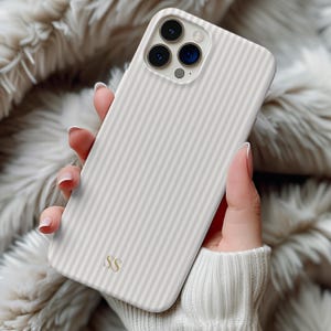Op de afbeelding: Een lichtgekleurde telefoonhoes met verticale strepen in een neutraal kleurenschema. De hoes heeft een gladde afwerking en heeft de initialen "SS" aan de onderkant. De telefoonhoes is ontworpen voor een smartphone en heeft uitsparingen voor de camera.