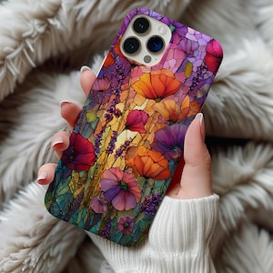 May include: A floral phone case featuring a stained-glass style design. The case showcases vibrant orange, purple, and red flowers with green foliage. The case is held in a person's hand, with a white sweater in the background.