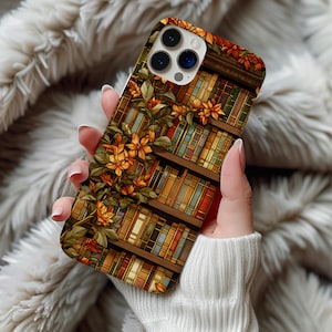 May include: A smartphone case featuring a printed design of wooden bookshelves filled with colorful books and climbing vines with orange flowers. The case has a cutout for a triple-lens camera system on the top left corner and a smooth finish.