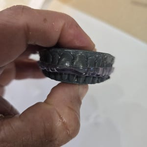 May include: A dark gray dental impression held in a hand. The impression is of a full set of teeth, with a clear, flexible plastic tray. The teeth are detailed and show the shape of the gums.