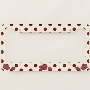 May include: Cream-colored license plate frame with a pattern of maroon polka dots and ladybug illustrations. The frame has a border of ladybug designs and is a decorative accessory for vehicles.