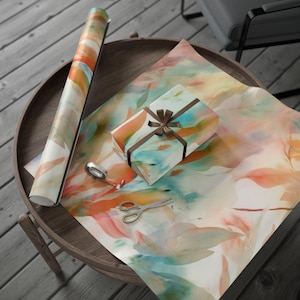 May include: A roll of gift wrap and a wrapped gift box with a brown ribbon sit on a wooden table. The gift wrap and box feature a watercolor design in shades of orange, teal, and brown. Scissors and tape are also on the table.