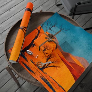 Op de afbeelding: Een cadeaupapier set met een oranje en blauw landschapsthema, inclusief een rol cadeaupapier, een ingepakt cadeau met een bruin lint en een vel cadeaupapier. Een schaar en plakband liggen ook op de tafel.