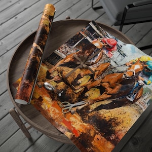 Könnte beinhalten: Eine Rolle Geschenkpapier und ein verpacktes Geschenk mit einem Gemälde eines Pferderennens. Das Papier und das Geschenk liegen auf einem Holztablett mit einer Schere und einer Rolle Klebeband. Das Gemälde hat braune, gelbe und weiße Farben.