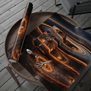 May include: A gift wrapped in space-themed wrapping paper with a brown ribbon, next to a roll of matching paper. Gold scissors and tape are on the wooden table. The paper design features swirling orange and black cosmic patterns.