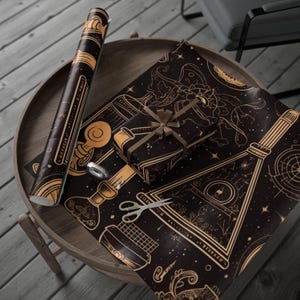 May include: Black and gold wrapping paper with a celestial design, featuring constellations and geometric shapes. A wrapped gift with a brown ribbon sits on the paper, along with a roll of the paper and scissors. The paper is on a wooden table.