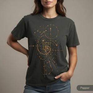 May include: A charcoal gray short-sleeve t-shirt featuring a gold-colored geometric graphic print on the front. The design consists of intricate intersecting circles, lines, and a central spiral pattern that resembles a mathematical golden ratio.