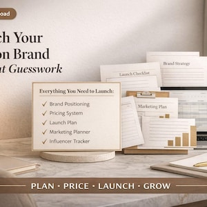 Puede incluir: Un espacio de trabajo con un portátil, un bloc de notas y documentos etiquetados como "Brand Strategy", "Launch Checklist" y "Marketing Plan". Un letrero enumera "Brand Positioning", "Pricing System", "Launch Plan", "Marketing Planner" e "Influencer Tracker". El texto "Launch Your Fashion Brand Without Guesswork" es visible.