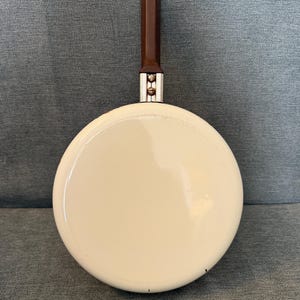 May include: A small, cream-colored frying pan with a dark brown handle. The pan has a rounded shape and a shiny surface. The handle is rectangular and attached to the pan with silver hardware. A vintage kitchenware item.
