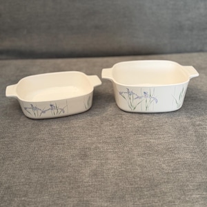 Pode incluir: Duas travessas quadradas em creme com pegas. Cada travessa apresenta um design floral com detalhes em azul e verde. As travessas estão vazias e sobre uma superfície cinzenta.