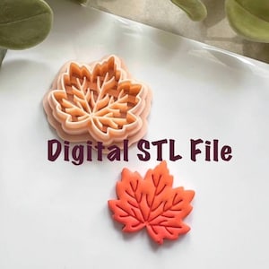 May include: A maple leaf-shaped cookie cutter and a leaf-shaped cookie. The cookie cutter is light orange and has a layered design. The leaf-shaped cookie is orange-red. The text "Digital STL File" is in the image.