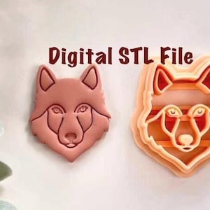 May include: Two wolf-shaped cookie cutters. One is a solid pink color, and the other is a layered orange design. The text "Digital STL File" is in brown letters above the cutters. These cutters are ideal for creating wolf-themed cookies or crafts.