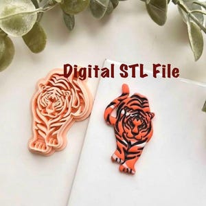 May include: Two tiger-shaped objects. One is a light orange cookie cutter, and the other is a painted tiger figurine in orange, black, and white. The text "Digital STL File" is in the upper right corner.
