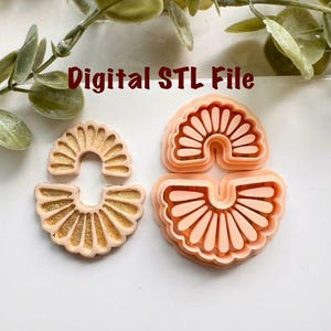 以下が含まれることがあります： 金色のものと桃色の、扇形のポリマークレイカッターが2つ。「Digital STL File」の文字。イヤリングやその他のジュエリー作りに使用。デザインは、放射線状のラインを持つ半円形です。