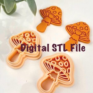 May include: Orange mushroom-shaped cookie cutters and finished cookies with a dotted cap design. The text "Digital STL File" is displayed in the image. The cutters are a light orange color.