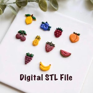 May include: A collection of colorful fruit-shaped miniatures, including a lemon, cherries, blueberries, pineapple, raspberry, peach, strawberry, grapes, banana, and watermelon. The text "Digital STL File" is displayed in a dark brown font. The fruits are arranged on a white surface.
