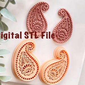Può includere: Sono esposti quattro oggetti a forma di paisley nelle tonalità del pesca e del rosa. Gli oggetti presentano dettagliati motivi floreali e a goccia. Il testo "Digital STL File" è stampato in colore rosso scuro.