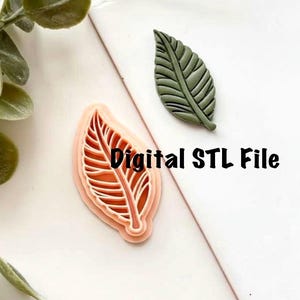 以下が含まれることがあります： 白い表面に、葉の形をした3Dプリントモールドと緑色の葉の形をしたオブジェクトが表示されています。 モールドは、詳細な葉のデザインが施されたピーチ色です。 画像には「Digital STL File」というテキストが印刷されています。
