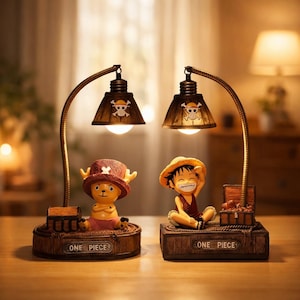 Puede incluir: Dos lámparas decorativas con personajes del anime One Piece. Cada lámpara tiene un brazo curvo de color bronce que sostiene una pantalla con un diseño de calavera y tibias cruzadas. Las bases dicen "ONE PIECE".
