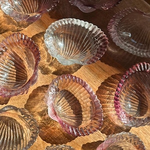 Könnte beinhalten: Eine Sammlung von Glasschalen in Muschelform, bestehend aus einer Mischung aus klarem Glas und durchscheinendem, rosafarbenem Glas. Jede Schale hat einen gewellten Rand und eine gerippte Textur, die von der Basis ausstrahlt.