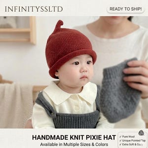 May include: A baby wearing a handmade knit pixie hat in a deep red colour. The hat has a unique pointed top and a rolled brim. The baby is also wearing a white collared shirt and grey overalls. The text "HANDMADE KNIT PIXIE HAT" is visible.