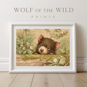 Op de afbeelding: Een ingelijste print met een aquarel illustratie van een Tasmaanse duivel die over een mosachtig blok kijkt. Het kunstwerk is omgeven door groen en witte bloemen, met de tekst "WOLF OF THE WILD PRINTS" bovenaan.