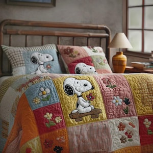 Puede incluir: Un edredón de retazos y dos almohadas a juego con diseños de Snoopy y flores. El edredón tiene una variedad de colores que incluyen amarillo, naranja, azul y rosa. El personaje de Snoopy sostiene una flor. La cama tiene un cabecero de madera.