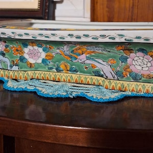 May include: A rectangular ceramic planter featuring a green background with hand-painted floral motifs, including pink and white peonies, orange blossoms, and a central bird figure. The rim has a white border with green wave patterns.