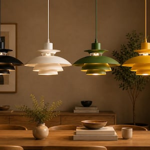 Peut inclure: Quatre suspensions à plusieurs niveaux alignées, chacune composée d'une série d'abat-jours incurvés superposés. Les luminaires sont finis en noir mat, blanc, vert olive et jaune moutarde, suspendus par des cordons assortis au plafond.