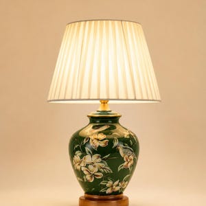 Peut inclure: Lampe de table décorative avec un pied en céramique vert orné de motifs floraux et d'oiseaux. L'abat-jour est plissé et la base est en bois. La lampe est conçue pour l'intérieur et ajoute une touche d'élégance à n'importe quelle pièce.