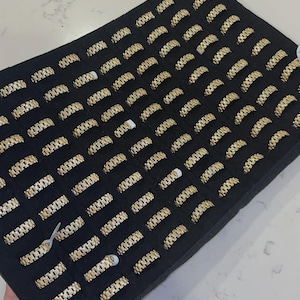 以下が含まれることがあります： 黒いベルベットの表面に並べられた金色の指輪のディスプレイ。リングはテクスチャ加工されたリンクデザインです。リングは黒いトレイに展示されており、手で持っています。