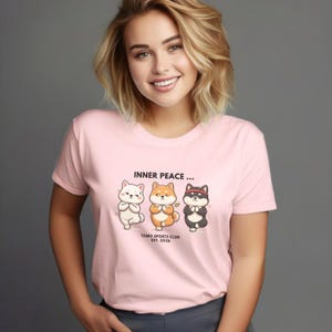 May include: A pale pink t-shirt with the words "INNER PEACE..." and three cartoon Shiba Inu dogs in yoga poses. The shirt also includes the text "TOMO SPORTS CLUB EST. 2026".