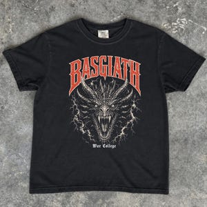 Puede incluir: Camiseta negra con un gr&aacute;fico de drag&oacute;n y la palabra "BASGIATH" en rojo encima. El texto "War College" est&aacute; debajo. El drag&oacute;n tiene dientes afilados y est&aacute; rodeado de rayos. Cuello redondo cl&aacute;sico.