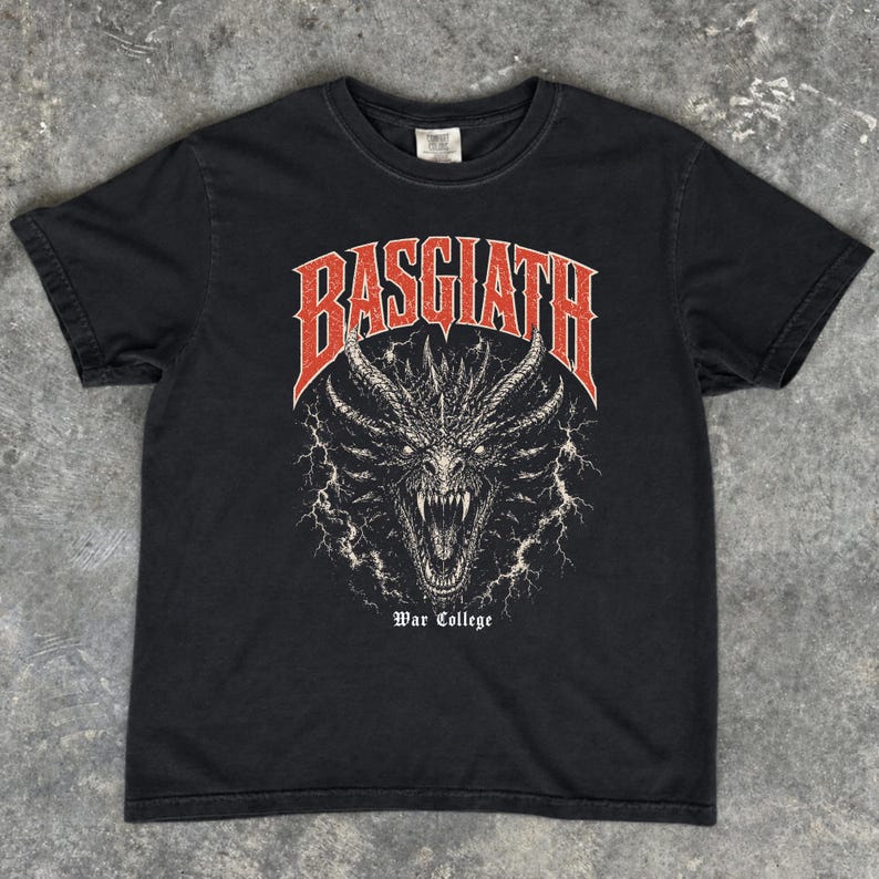 Puede incluir: Camiseta negra con un gr&aacute;fico de drag&oacute;n y la palabra "BASGIATH" en rojo encima. El texto "War College" est&aacute; debajo. El drag&oacute;n tiene dientes afilados y est&aacute; rodeado de rayos. Cuello redondo cl&aacute;sico.