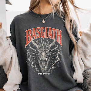 Puede incluir: Camiseta gris oscuro con un gr&aacute;fico rojo y blanco de una cabeza de drag&oacute;n y la palabra "BASGIATH" encima. El texto "War College" est&aacute; debajo. La camiseta tiene un aspecto vintage y desgastado.