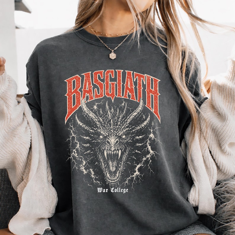 Puede incluir: Camiseta gris oscuro con un gr&aacute;fico rojo y blanco de una cabeza de drag&oacute;n y la palabra "BASGIATH" encima. El texto "War College" est&aacute; debajo. La camiseta tiene un aspecto vintage y desgastado.